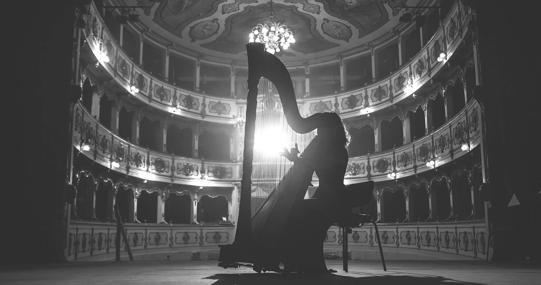 Cinematic shot of Female Harpist Playing Harp Solo on an Empty Classic Theatre Stage with Dramatic Lighting. Professional Musician Rehearsing Before the Start of a Big Show. Silhouette Aesthetics