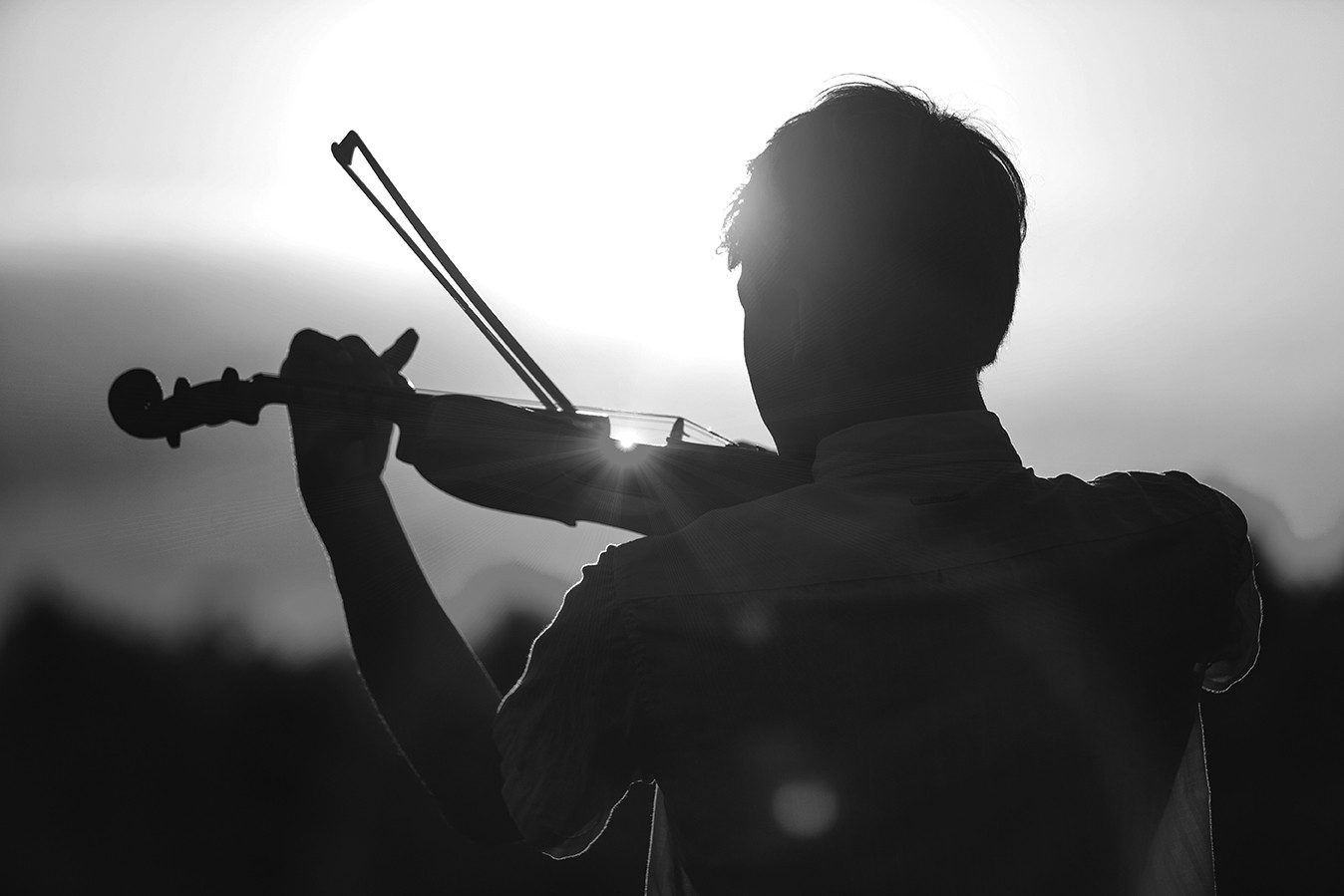 Young man or boy playing the violin at sunset standing with his back to the camera with his instrument and bow silhouetted against the fiery orange sky