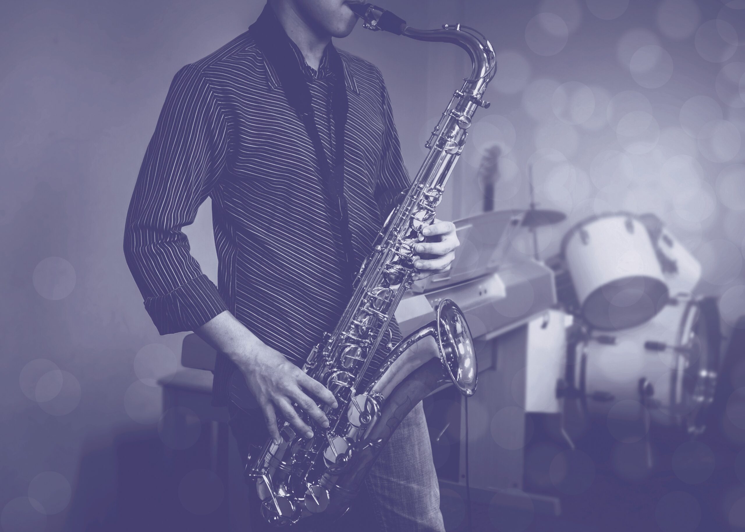 young musician man plays tenor saxophone on stage with light bokeh effected over  blurred music instrument background